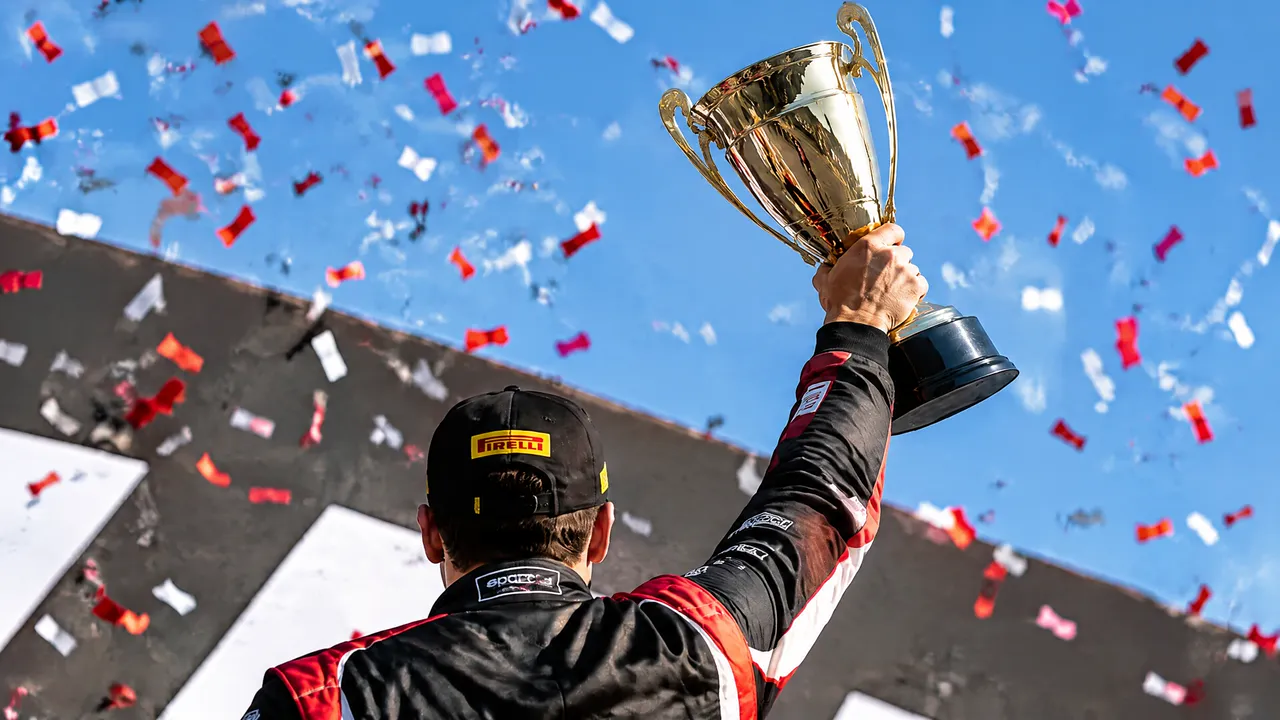 A racing driver lifting a gold trophy under confetti